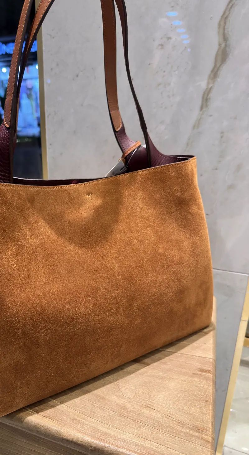 A tan suede tote seen from the side, showing its soft shape