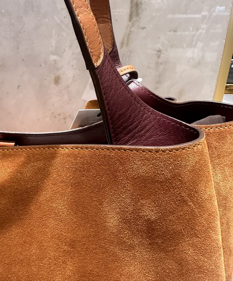 Close-up of a suede tote showing the burgundy leather lining and stitched handle