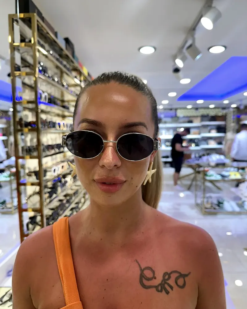 A visitor trying on round sunglasses in front of the sunglasses wall