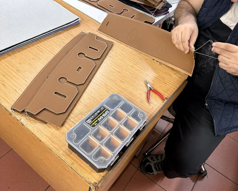 A craftsman hand-finishing a stitched leather panel at a workbench, with cut pattern pieces beside him